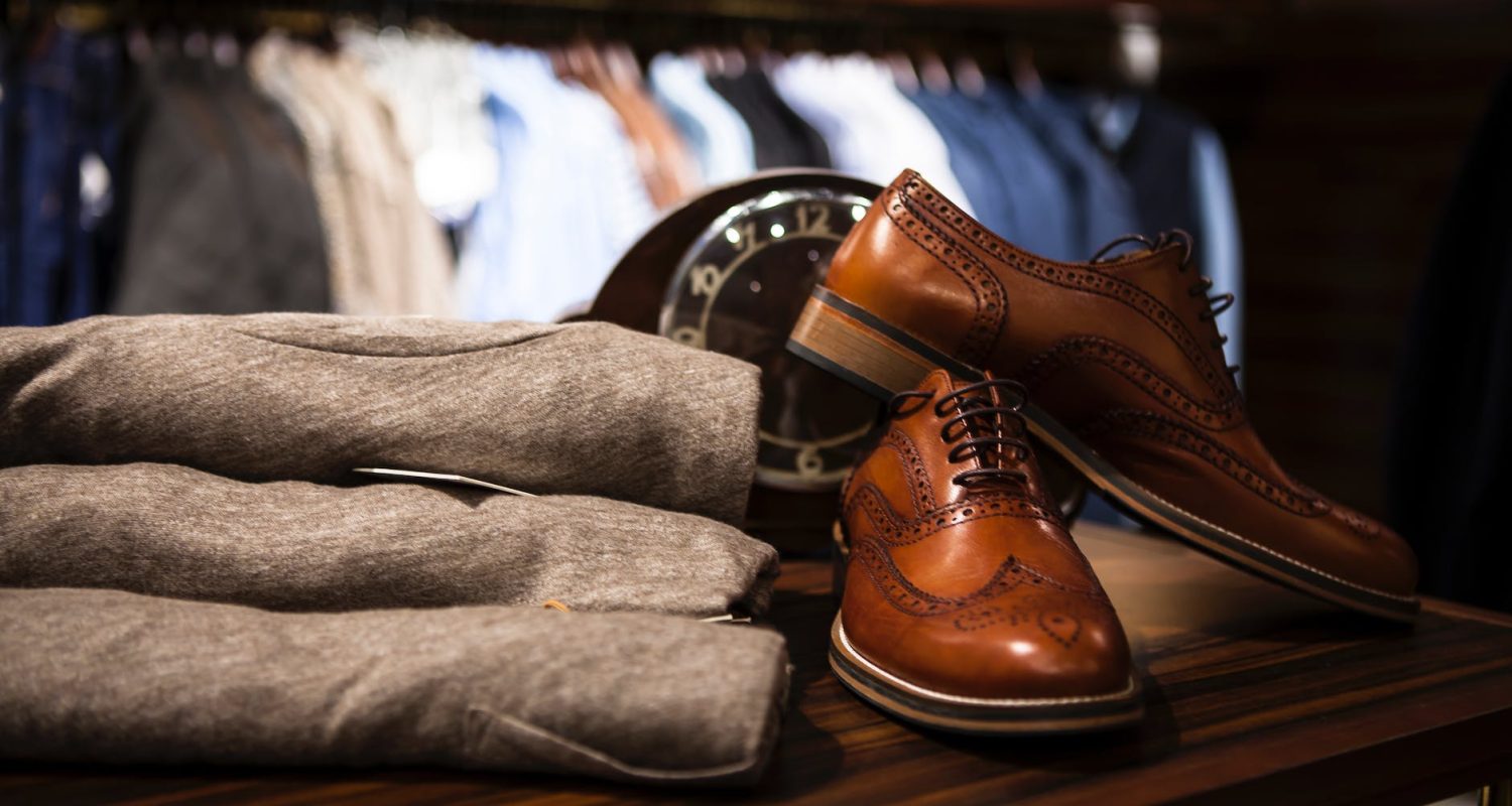 pair of brown leather wingtip shoes beside gray apparel on wooden surface